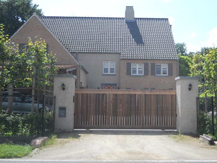 Houten schuifpoort met verticale houten bekleding tussen gemetselde poortpalen bij een vrijstaande woning